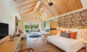 Et elegant hotellrom med seng, sitteområde og utsikt over hagen gjennom skyvedører. (AI-generert tekst)