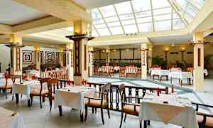 En romslig restaurant med store vinduer og bord med hvitduker. (AI-generert tekst)