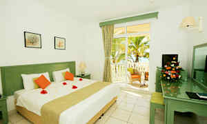 Hvitt rom med en stor seng, dekorative blomsterblader på dynen og terrasseutgang mot en palmehage. (AI-generert tekst)