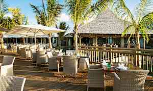 Utendørsrestaurant med bord og stoler på en treterrasse omgitt av palmer. (AI-generert tekst)