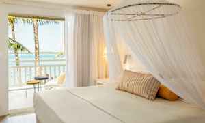 En lys hotellsuite med himmelseng og utsikt over havet fra balkongen. (AI-generert tekst)