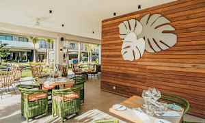 En utendørsrestaurant med grønne møbler og en veggdekorasjon med store blader. (AI-generert tekst)