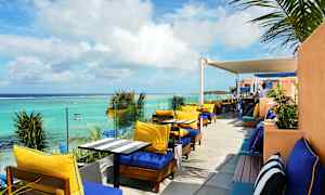 Uteservering med solsenger og bord ved havet. (AI-generert tekst)