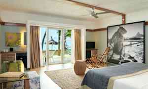 Et hotellrom med moderne interiør, glassdører som åpner mot strand og palmetrær. (AI-generert tekst)