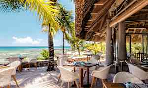 En strandrestaurant med sitteplasser utendørs og utsikt over havet. (AI-generert tekst)