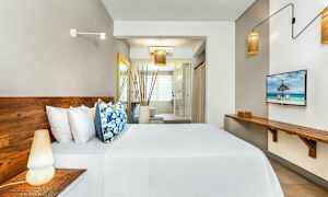 Bilde av et moderne hotellrom med tremøbler, seng med hvite laken og fargerike puter, og et stort vindu i bakgrunnen. (AI-generert tekst)