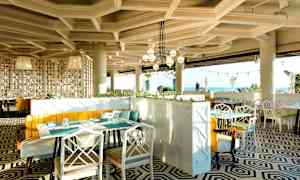 En moderne restaurant med geometrisk mønstret gulv, lyse møbler og store panoramavinduer med utsikt mot havet. (AI-generert tekst)