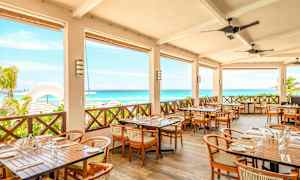 Restaurant med terrasse med bord og stoler, utsikt over havet og stranden. (AI-generert tekst)