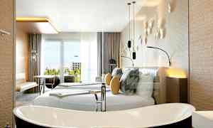 Et moderne hotellrom med en stor dobbeltseng, dekorative puter og veggdekorasjoner. Det finnes et frittstående badekar og møbler som bord og stoler nær en glassdør med utsikt. (AI-generert tekst)