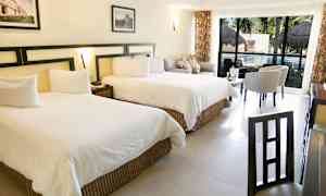 Bilde av et hotellrom med to store senger, sitteområde og et bord foran store vinduer som vender mot et basseng. (AI-generert tekst)