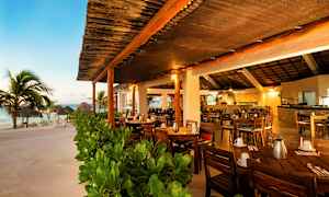 En restaurant med utendørs atmosfære og tremøbler ved stranden, omgitt av grøntområder. (AI-generert tekst)