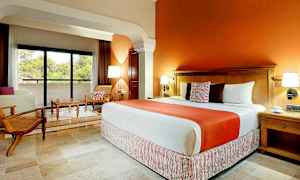 Hotellrom med en stor seng, to komfortable stoler, et bord og en balkong med utsikt over grøntområde. (AI-generert tekst)