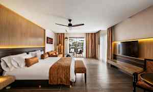 Hotellrom med stor seng, sittegruppe og utsikt gjennom glassdører. (AI-generert tekst)