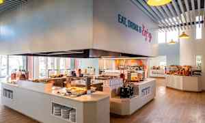 En kafeteria med selvbetjening, hvor mat presenteres på disker og brødutvalg vises på hyller. (AI-generert tekst)