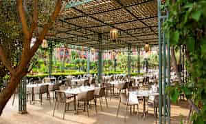 En utendørs servering med bord og stoler under et trebelagt tak. (AI-generert tekst)