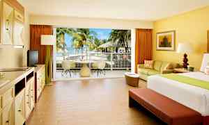 Hotelrom med lyst interiør og utsikt mot en terrasse med palmer og hav. (AI-generert tekst)