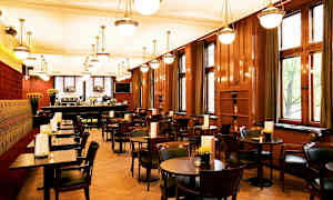 Bilde av en restaurantinteriør med trebord og stoler, store vinduer og hengende lamper i taket. (AI-generert tekst)