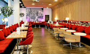 Stemningsfull restaurant med røde sitteplasser, små bord og en bakgrunnsvegg med et svart-hvitt bybilde. (AI-generert tekst)