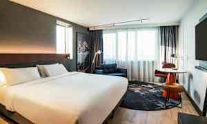 Et moderne hotellrom med en stor dobbeltseng, lenestol og et skrivebord ved vinduet. (AI-generert tekst)