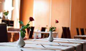 Et elegant dekket spisebord pyntet med en hvit vase som inneholder en enkelt rød rose. (AI-generert tekst)