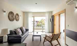 En moderne stue med sofa, trestol og tilgang til balkong gjennom glassdører. (AI-generert tekst)