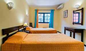 Et hotellrom med to enkeltsenger, et veggspeil, skrivebord og vindu med fargerike gardiner. (AI-generert tekst)