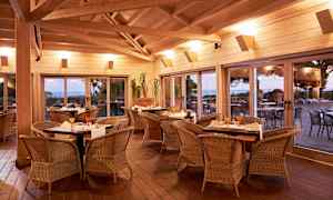 Innendørs miljø med spisebord og stoler av rotting, store vinduer med utsikt mot en terrasse og landskap utenfor. (AI-generert tekst)