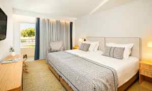 Hotellrom med to enkeltsenger, en stol, et arbeidsbord og en TV, samt et vindu med gardiner. (AI-generert tekst)