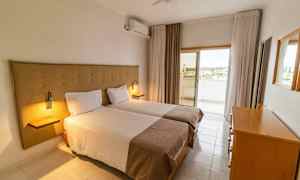 Et hotellrom med to enkeltsenger, en kommode og en utgang til en balkong. (AI-generert tekst)