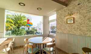 En kafé med et rundt bord og stoler nær et vindu som viser en palme og en bygning utenfor. (AI-generert tekst)