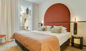 Moderne hotellrom med dobbeltseng, rødt sengegavl og store vinduer mot en balkong. (AI-generert tekst)