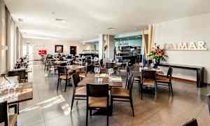 En lys og moderne restaurant med bord og stoler pent arrangert, friske blomster og store vinduer. (AI-generert tekst)