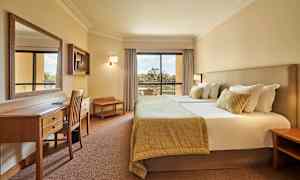 Bilde av et hotellrom med en dobbeltseng, skrivebord og stoler samt en balkong med utsikt. (AI-generert tekst)