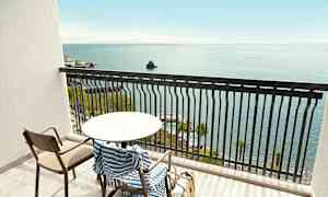 En balkong med bord, stol og stripete håndkle, med havutsikt. (AI-generert tekst)