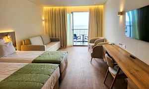 Et hotellrom med to senger, sofa, to lenestoler, skrivebord og en balkong med utsikt. (AI-generert tekst)