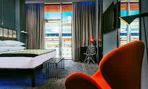 Moderne hotellrom med stor seng, skrivebord og stol samt utsikt gjennom store vinduer. (AI-generert tekst)