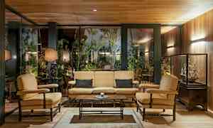 Interiør med sittegruppe bestående av sofa og lenestoler foran en glassvegg med vegetasjon utenfor. (AI-generert tekst)