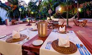 Vakkert opplyst utendørs serveringsplass med dekket bord og palmer i bakgrunnen. (AI-generert tekst)