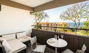 En terrasse med sittegruppe og utsikt mot havet, med bord og to glass vin. (AI-generert tekst)