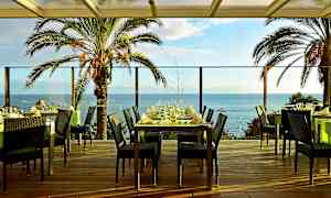 Restaurantbord på en terrasse med utsikt over havet og palmer. (AI-generert tekst)