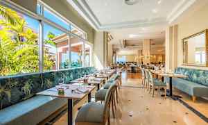 En lys restaurant med moderne bord og stoler samt store vinduer med utsikt over grøntområder. (AI-generert tekst)