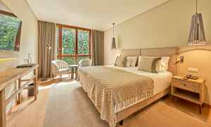 Et hotellrom med en bred seng, to lenestoler ved et vindu og et bord. (AI-generert tekst)