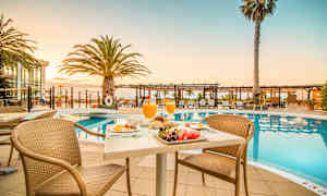 Et frokostbord ved et basseng med solsenger og palmer i bakgrunnen. (AI-generert tekst)