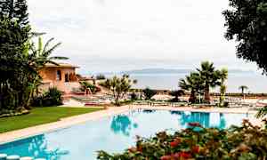 Bilde av et utendørsbasseng omgitt av grøntområder, med solsenger og en bygning i bakgrunnen. (AI-generert tekst)