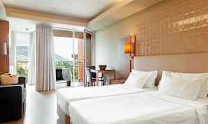 Hotellrom med to enkeltsenger, sittegruppe og utsikt mot et fjellområde gjennom glassdøren. (AI-generert tekst)