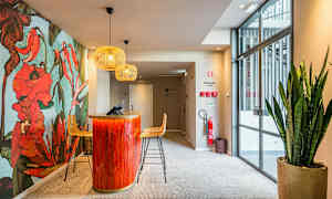 Resepsjon med en dekorativ blomstervegg, rød-oransje resepsjonsdisk og sitteplasser med moderne lamper over. (AI-generert tekst)