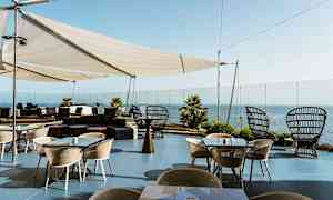 Utendørsterrasse med bord og stoler, pergola og havutsikt. (AI-generert tekst)