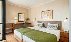 Bilde av et hotellrom med to enkeltsenger kledd i hvitt sengetøy og grønne overkast, et skrivebord med speil og en stol i bakgrunnen. (AI-generert tekst)