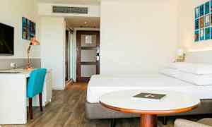 Hotellrom med en seng, skrivebord og stål, samt et rundt bord foran sengen. (AI-generert tekst)