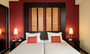 To senger med hvitt sengetøy og røde puter, en vegg med trepaneler og rød bakgrunn. (AI-generert tekst)